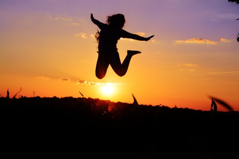 happy, silhouette-of-woman-jumping-in-meadow-at-sunset